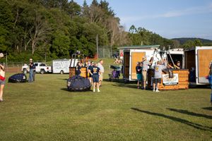 Food trucks and vendor stalls lined up at an outdoor event with trees in the background.
