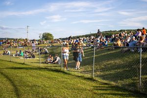 Large crowd seated on a hillside watching an outdoor event under blue skies.