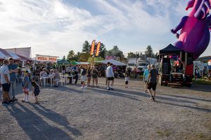 Festival goers walking between vendor stalls and food trucks at dusk.
