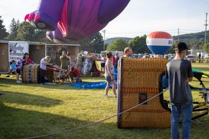 A vibrant purple hot air balloon being set up at an outdoor festival with equipment and crew.