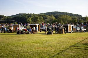 Large crowd gathered on a grassy field for a hot air balloon festival with hills in the background.