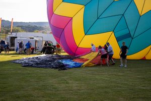 Crew members work to prepare a large colorful patterned hot air balloon on grass field.
