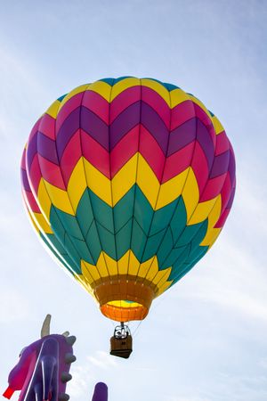 Bright multicolored hot air balloon with chevron pattern design floating against blue sky.