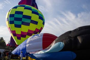 Colorful checkered hot air balloons being inflated at morning festival setup.