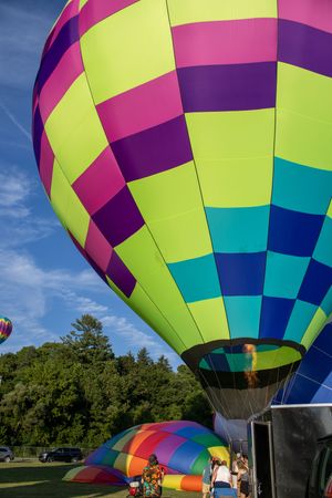 Vibrant neon hot air balloon with geometric pattern stands tall against blue summer sky.