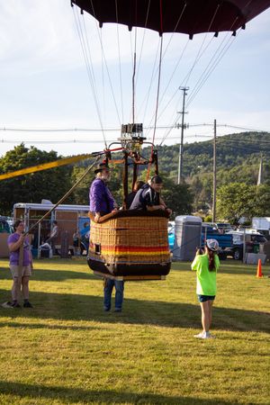 Hot air balloon basket tethered to ground as passengers prepare for flight at festival.