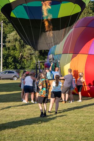 Hot air balloon crew preparing colorful balloons for launch on a grassy field.