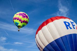 Multicolored hot air balloons floating in a clear blue sky during a festival.