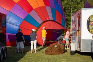 Ground crew working to inflate large red and multicolored hot air balloons on grass.