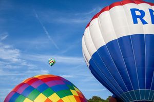 Hot air balloons with blue and white patterns ascending into bright blue sky.