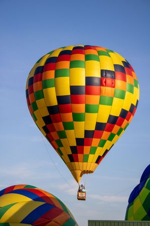 Yellow and red checkered hot air balloon floating in clear blue sky.