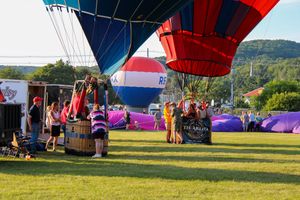 Vibrant hot air balloons lined up on a grassy field during a balloon festival with mountains in the background.