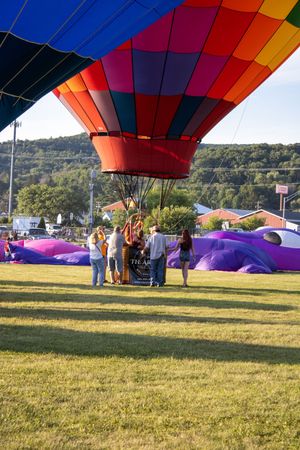 Colorful hot air balloons being inflated on a sunny day with rolling hills in the distance.