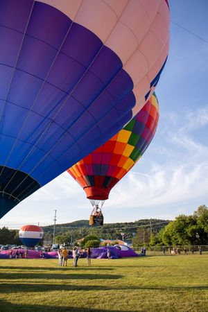 A large purple and rainbow-colored hot air balloon being prepared for launch in a green field.