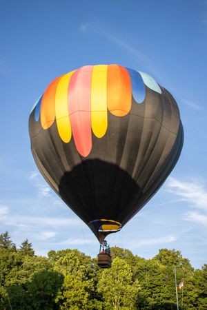 A black hot air balloon with orange and yellow accents rises against a bright blue sky.