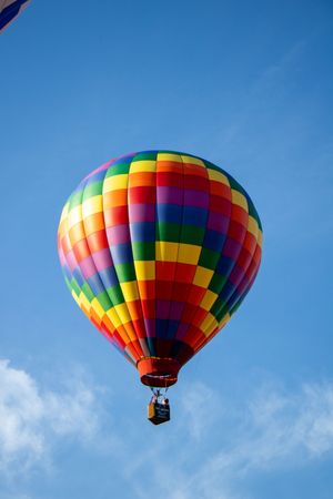 A rainbow-colored hot air balloon soars through clear blue skies during a festival.