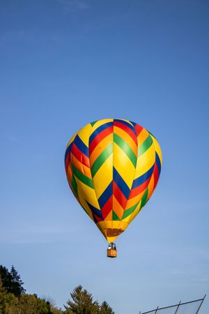 A bright geometric-patterned hot air balloon with yellow and red colors floats in a clear blue sky.