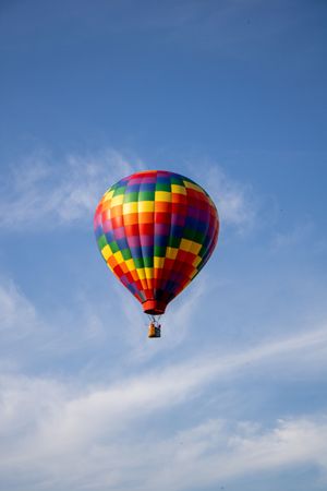 Vibrant rainbow-colored hot air balloons drift through wispy clouds in a bright blue sky.