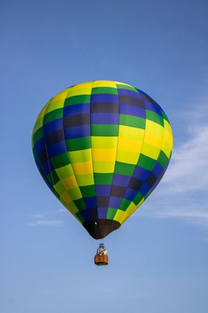 Hot air balloon with geometric pattern in yellow, green and blue against bright sky.