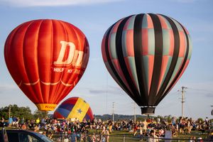 Row of inflated hot air balloons preparing for launch at outdoor festival.