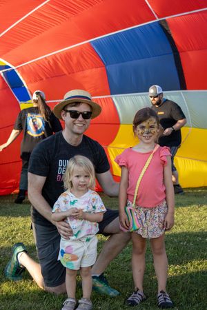 Spectators gathered near colorful hot air balloon at outdoor festival.