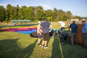 Festival attendees watching hot air balloons from grassy viewing area.