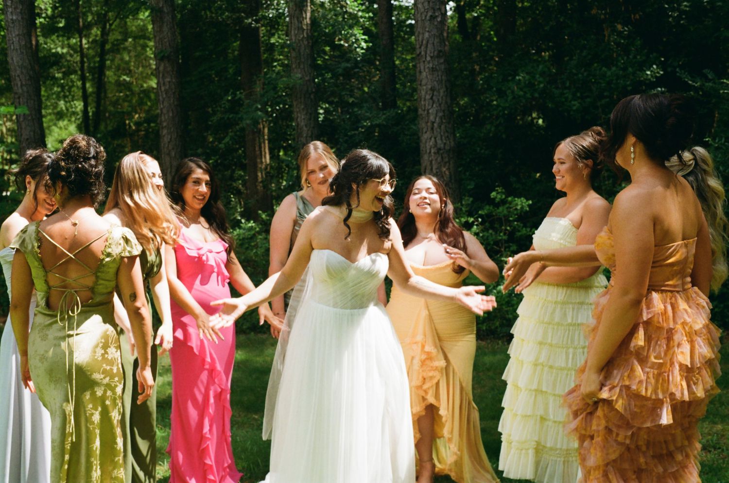 Bridesmaids in pastel and earth-toned dresses stand together outdoors in a wooded area, shot on 35mm film in Lancaster SC at The Ivy Place