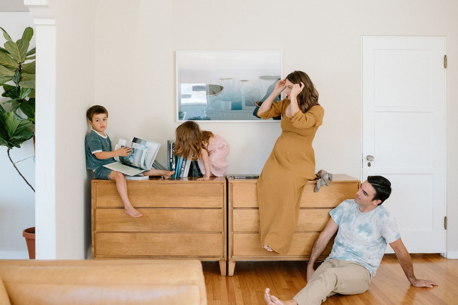 Family group playing and lounging together on wooden dresser and floor in bright minimalist bedroom.