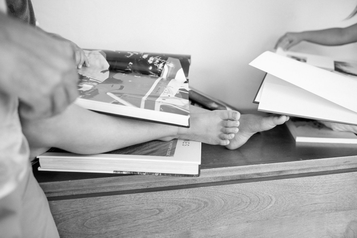 Hands sorting through papers and books on a wooden desk surface shown in black and white photography.