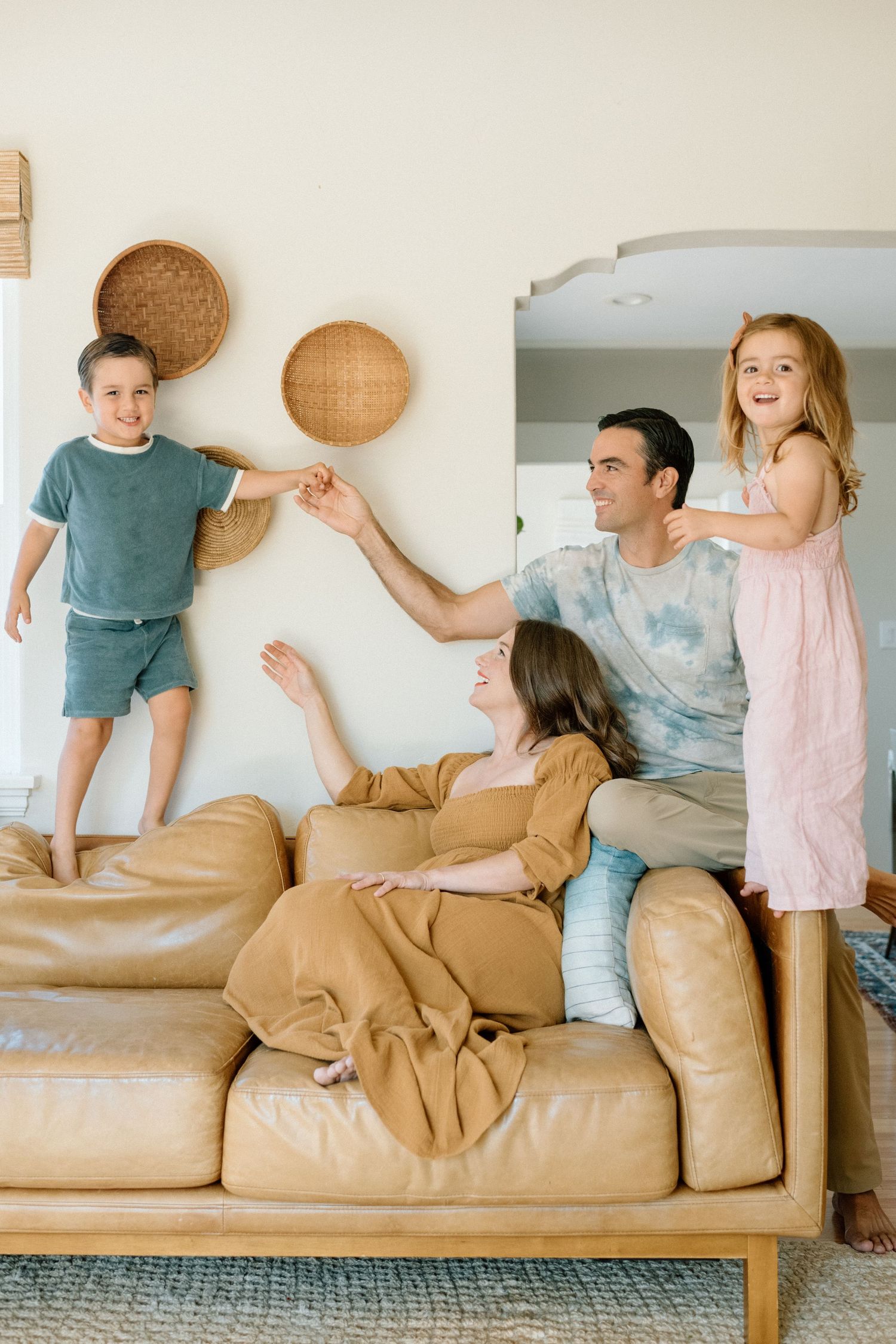 A joyful group playing and lounging on a tan leather couch with woven baskets decorating the wall behind them.