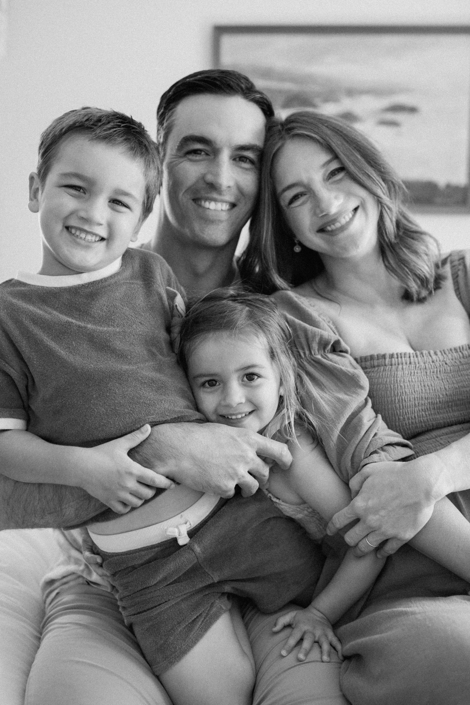 A series of black and white photos showing loving family moments of parents and children cuddling together in bed.