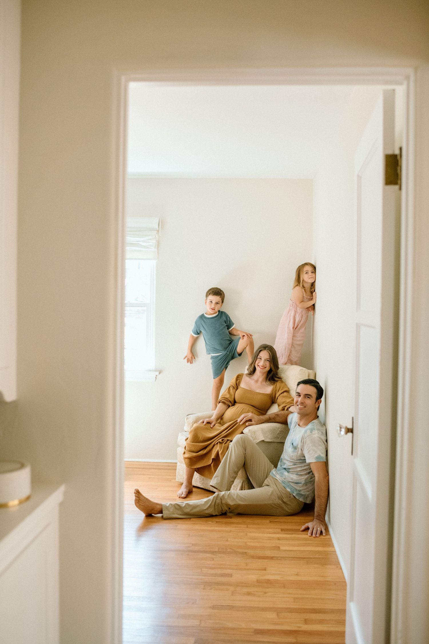Group of people sitting casually on hardwood floor in bright minimalist hallway or room with white walls.