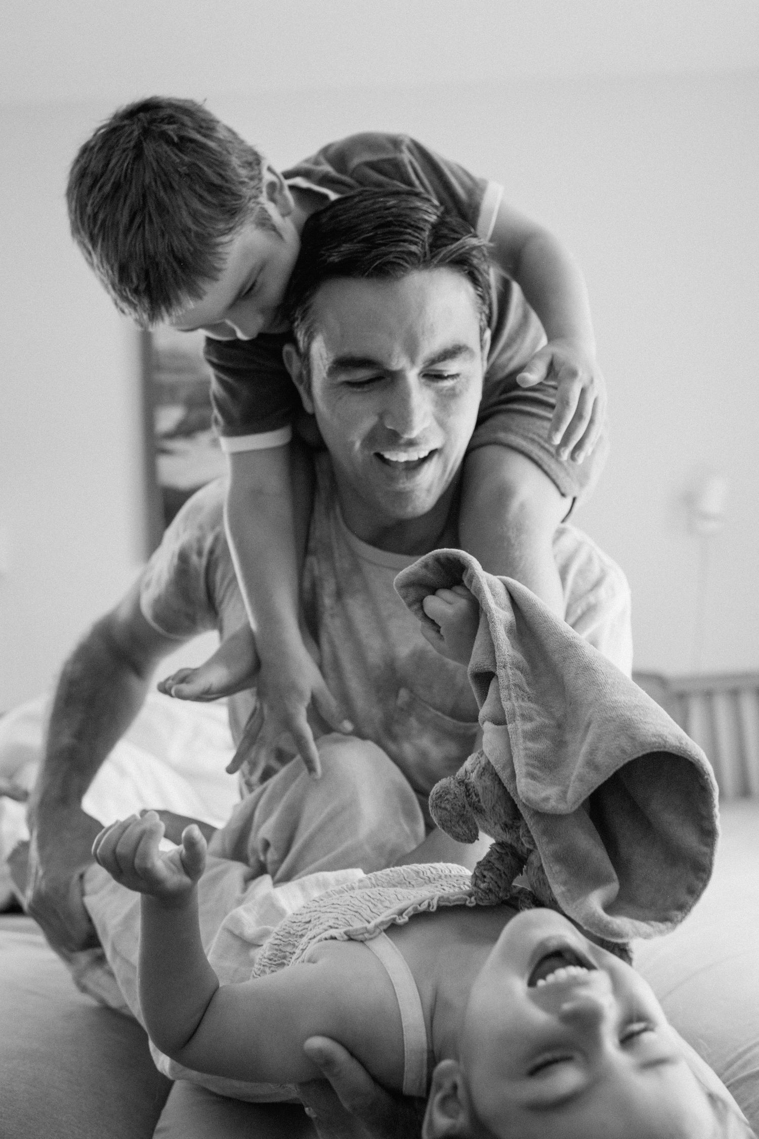 A candid black and white photo capturing a playful moment between people laughing and having fun on a bed.