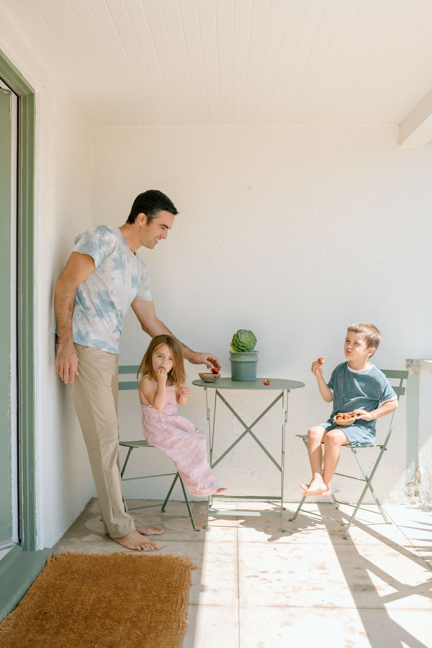 A sequence of someone in a bright room interacting with a pink-clad child near a metal folding table and chair.