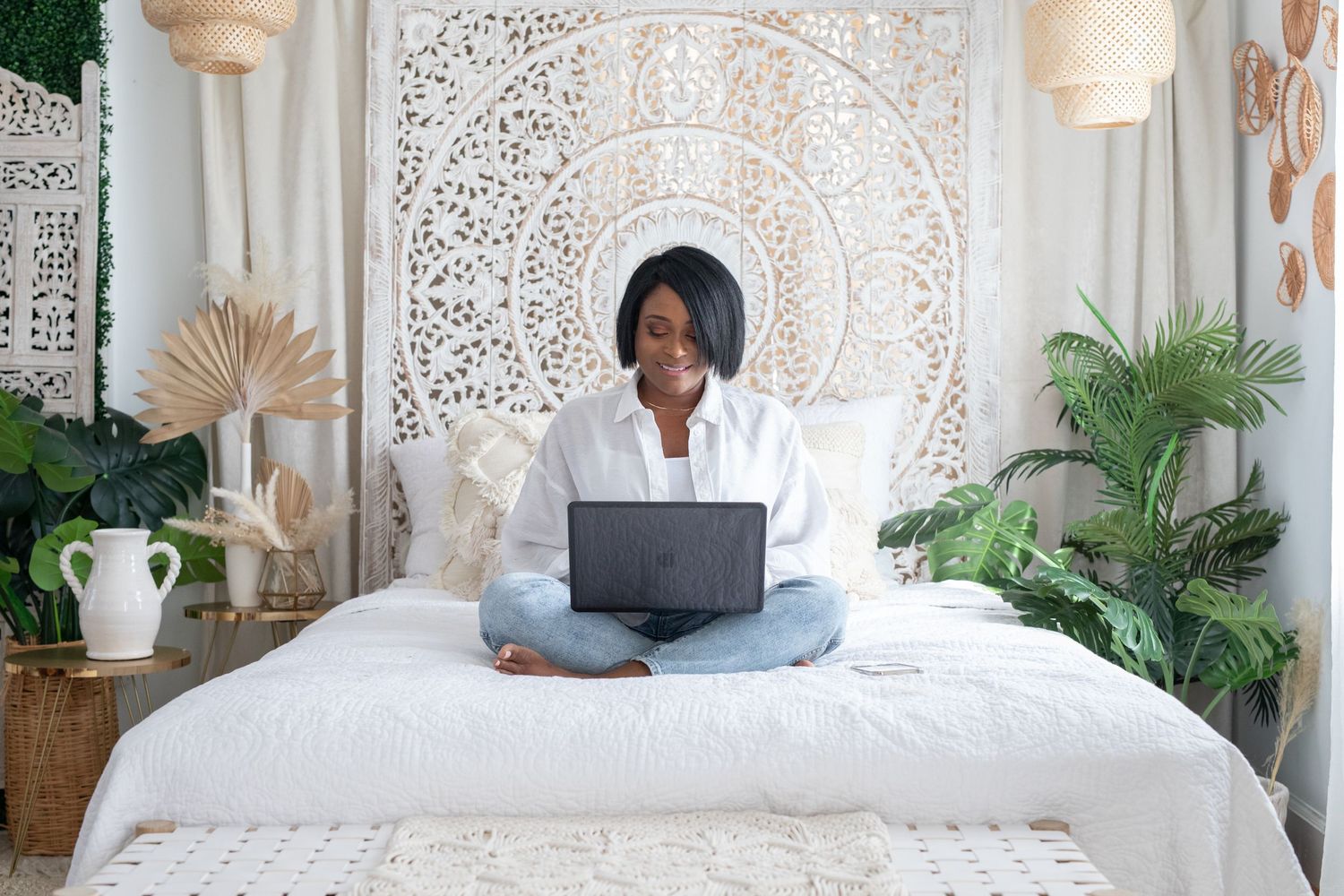 Stylish white living room setup with macrame decorations, woven pouf ottoman and boho-inspired decor elements.