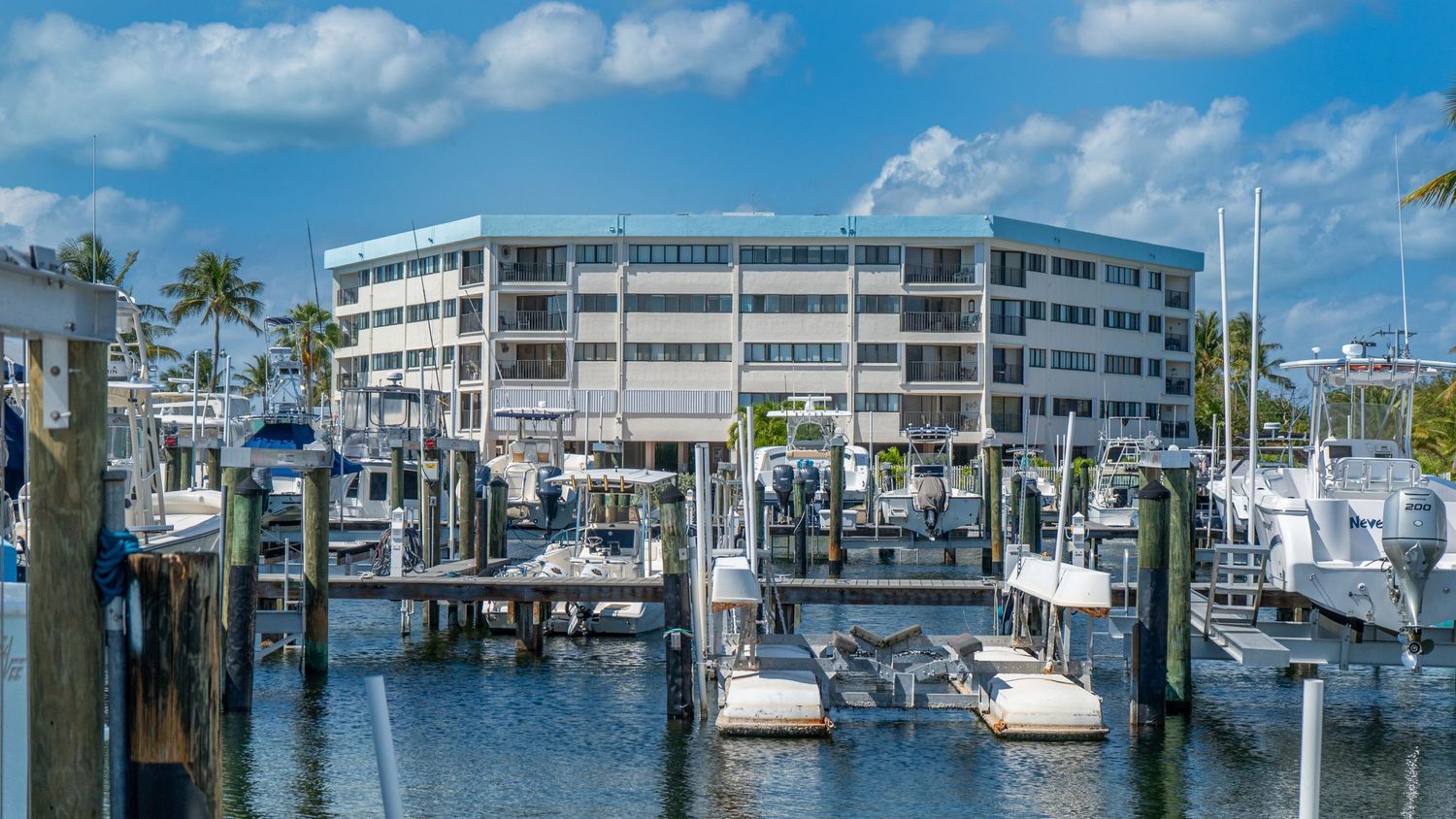 Marina with luxury yachts and condominiums along the waterfront under blue skies.