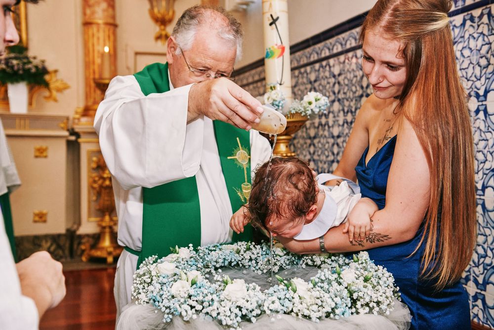 Catholic priest pouring holy water over a baby's head during a baptism ceremony at a church altar.