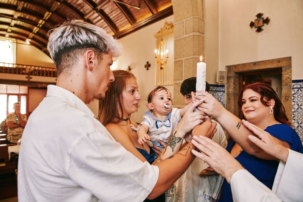 Family and godparents lighting a baptismal candle together during a Catholic christening ceremony in a church.
