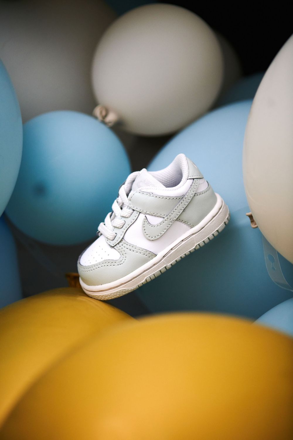 Small white Nike baby sneaker surrounded by blue, white, and yellow balloons.
