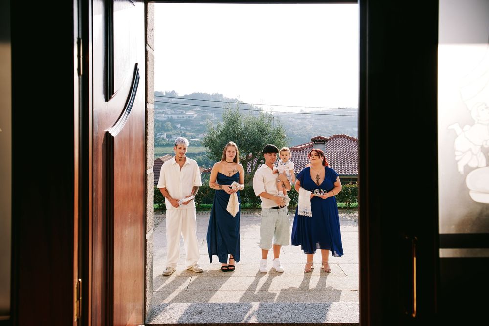 Group of family members in blue and white outfits arriving through wooden church doors for baptism ceremony.