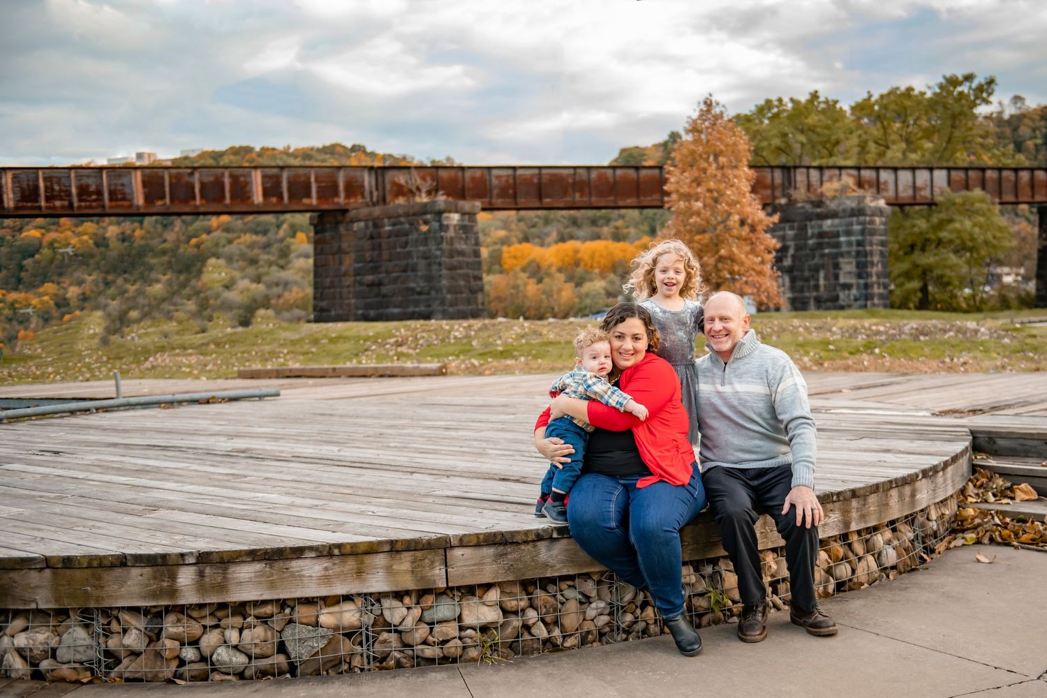 A group rests on a stone wall near train tracks with autumn foliage and mountains in the background.