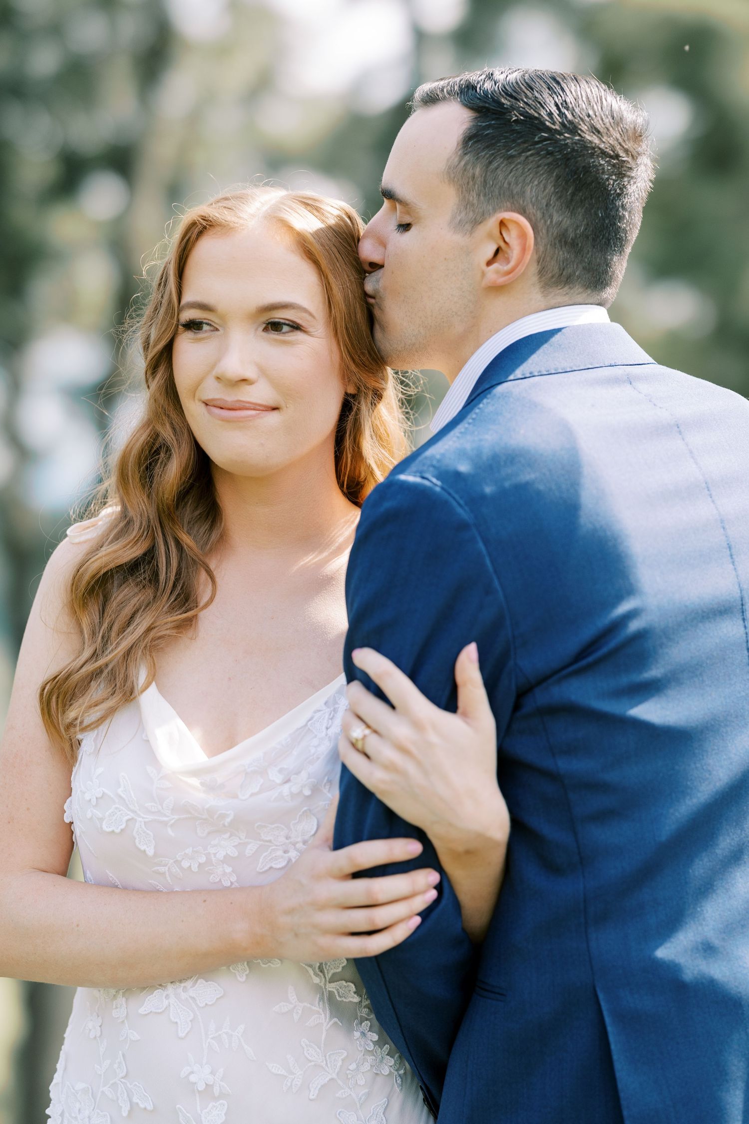 A romantic wedding portrait with a bride in a white lace gown and groom in navy suit embracing outdoors at Pendry Natirar in Peapack, NJ.