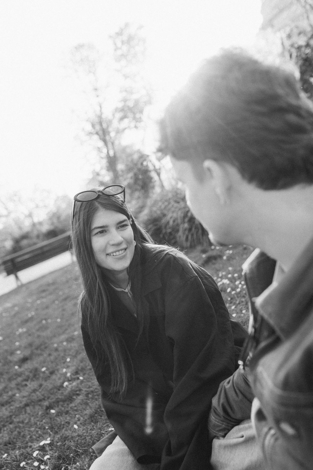 Candid black and white photo sequence showing two people sitting on grass sharing playful laughs together.