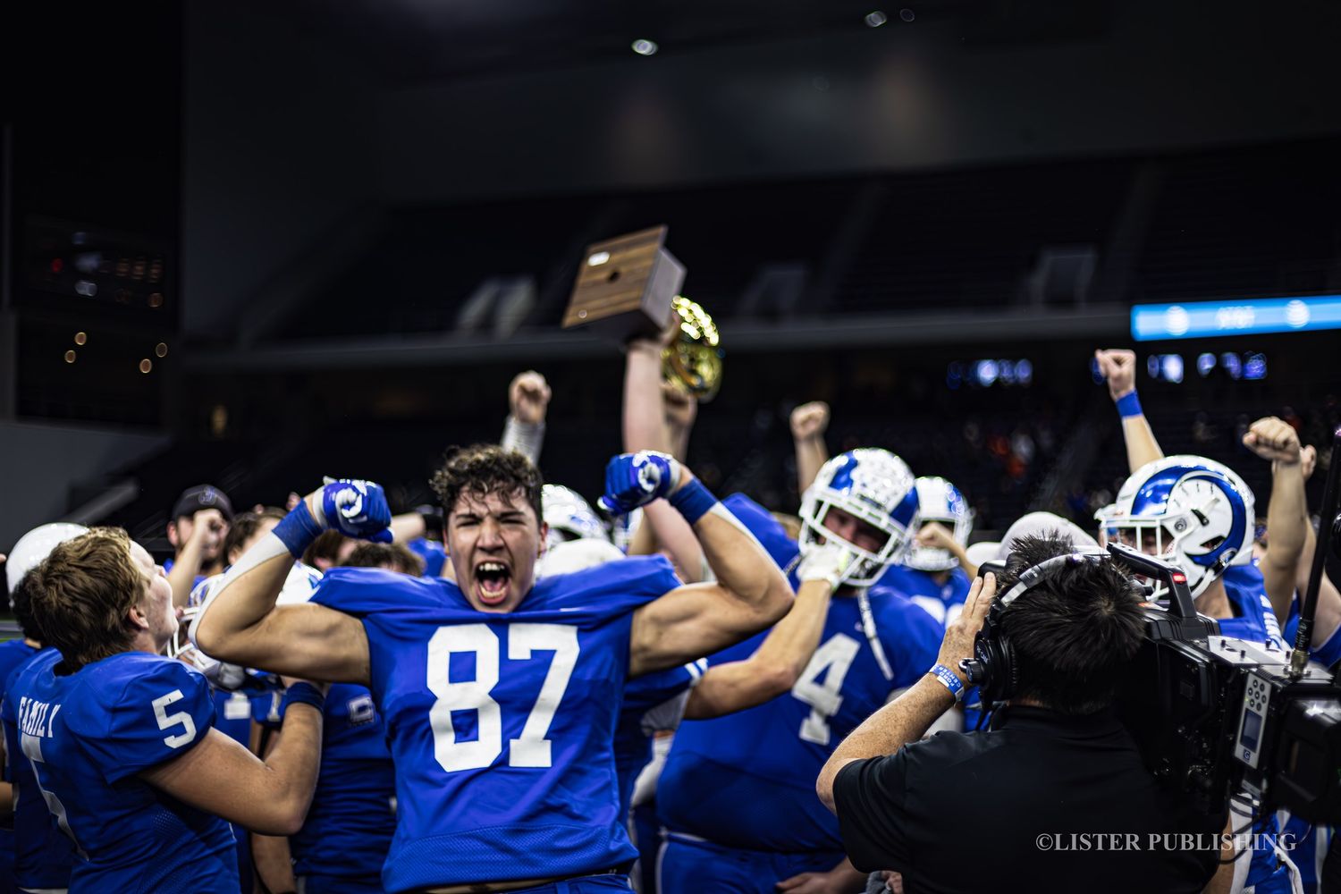 Football players in blue jerseys celebrating victory with raised arms in stadium.