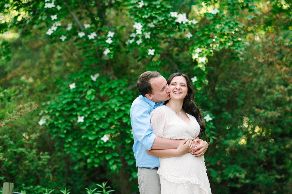 A couple shares a tender moment while hugging outdoors in a sunny garden.