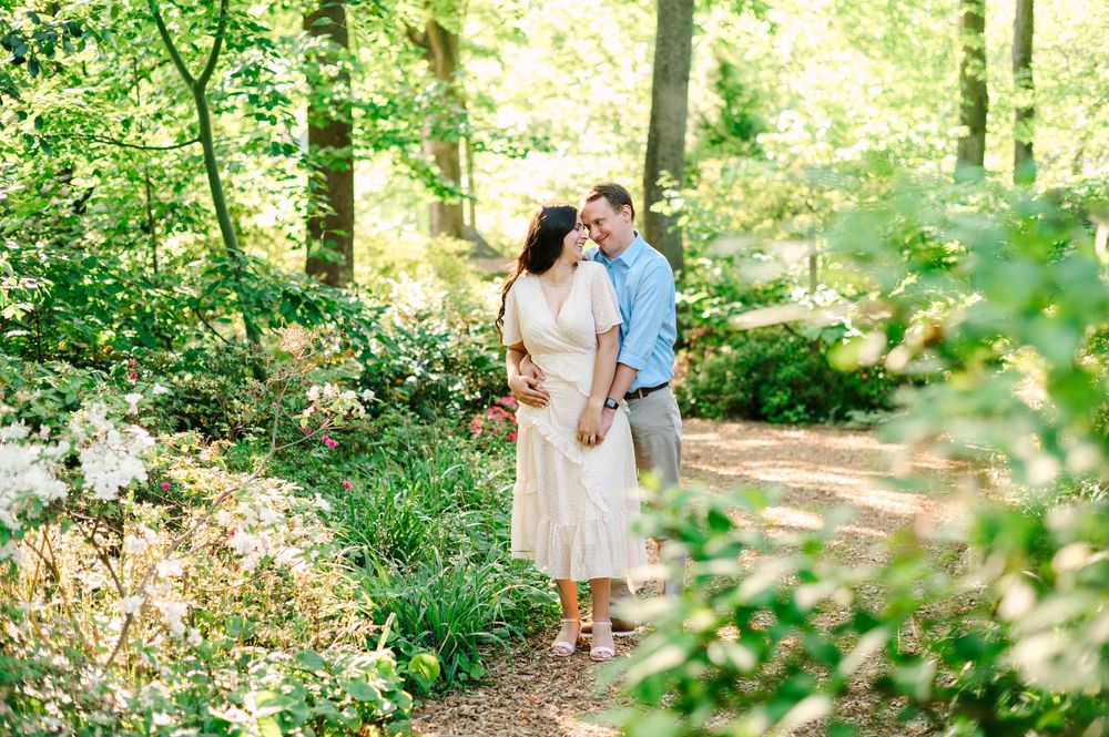 A couple strolls together on a garden path surrounded by flowering bushes and trees.