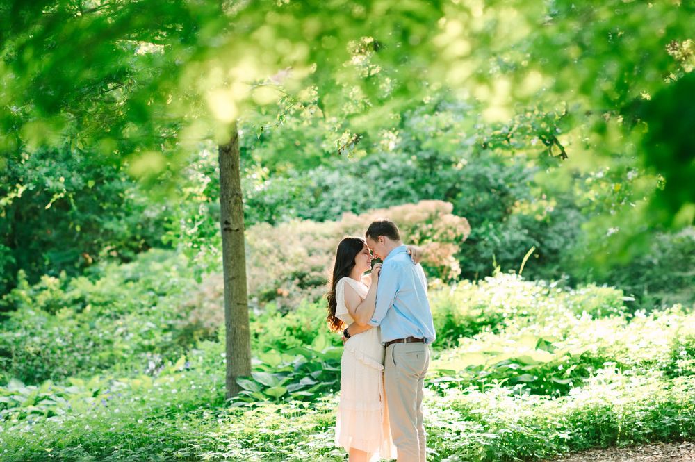 A couple shares an intimate moment in a verdant garden setting with dappled sunlight.