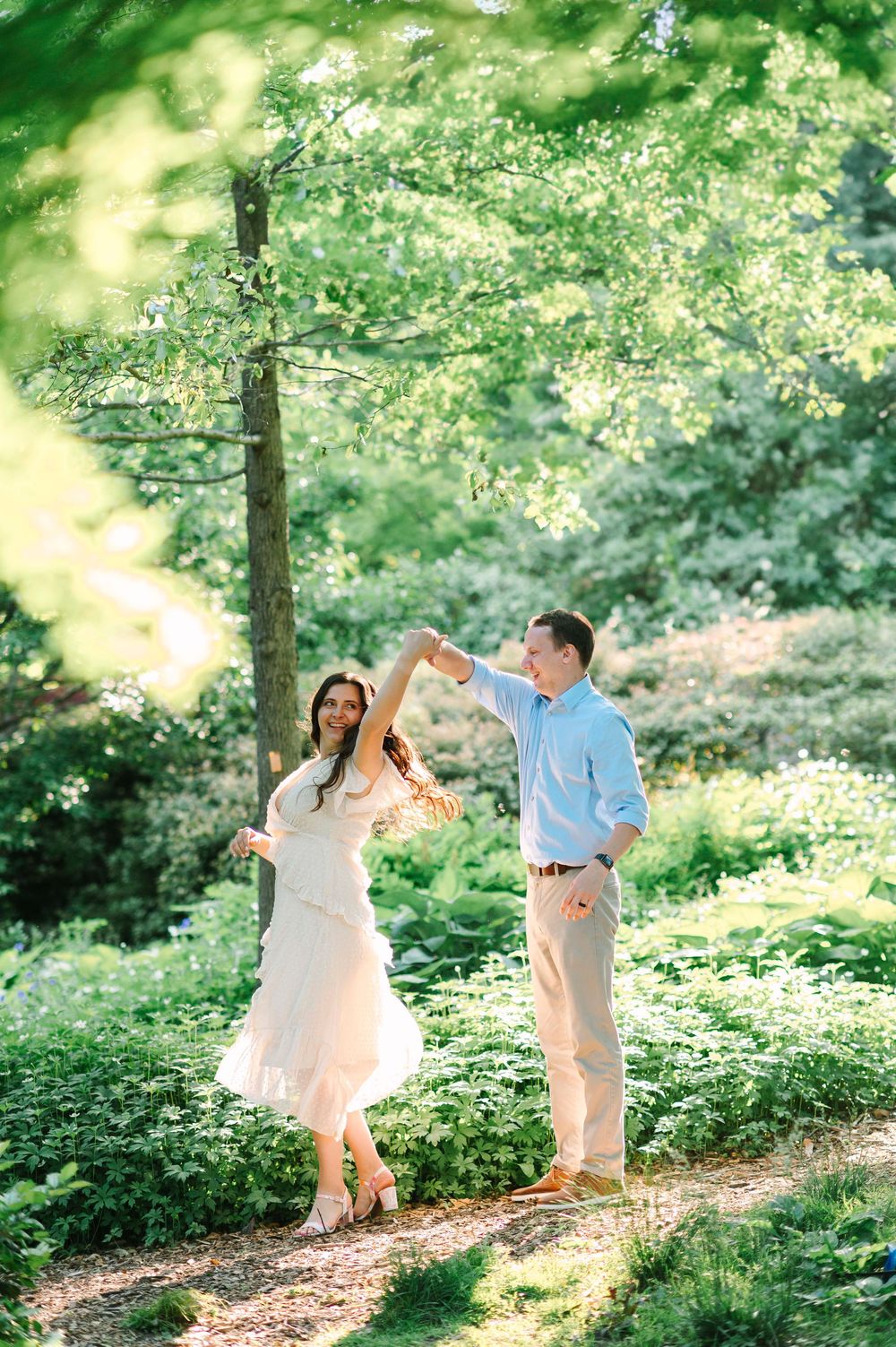 A couple dances playfully on a garden path beneath blooming trees.
