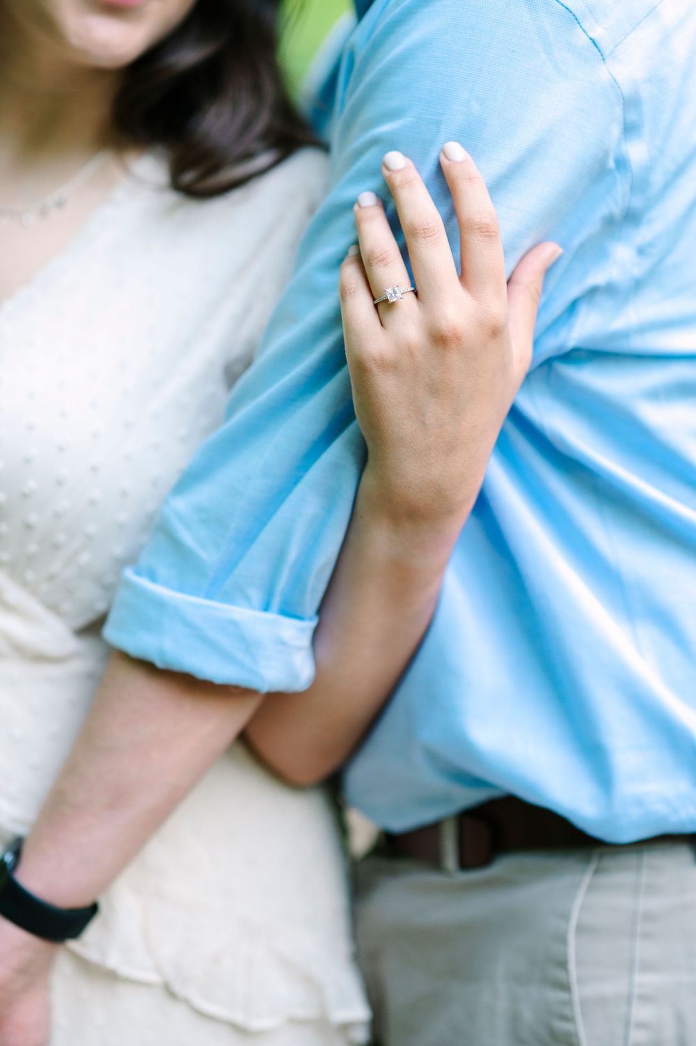 A close-up of an engagement ring as a couple embraces in soft natural light.