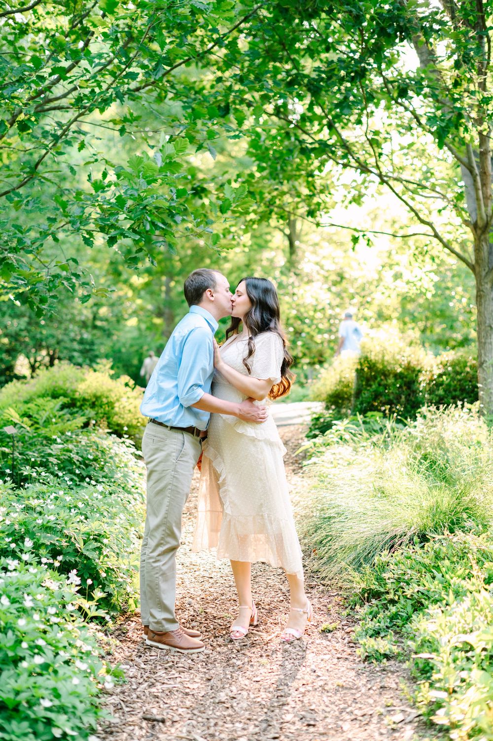 A couple sharing a tender moment on a nature trail surrounded by verdant summer foliage.
